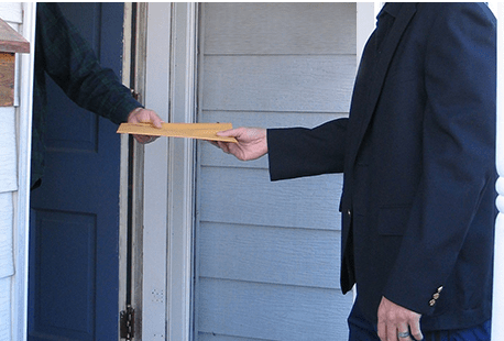 A person in a blazer receiving an envelope from another person's hand at a doorway.